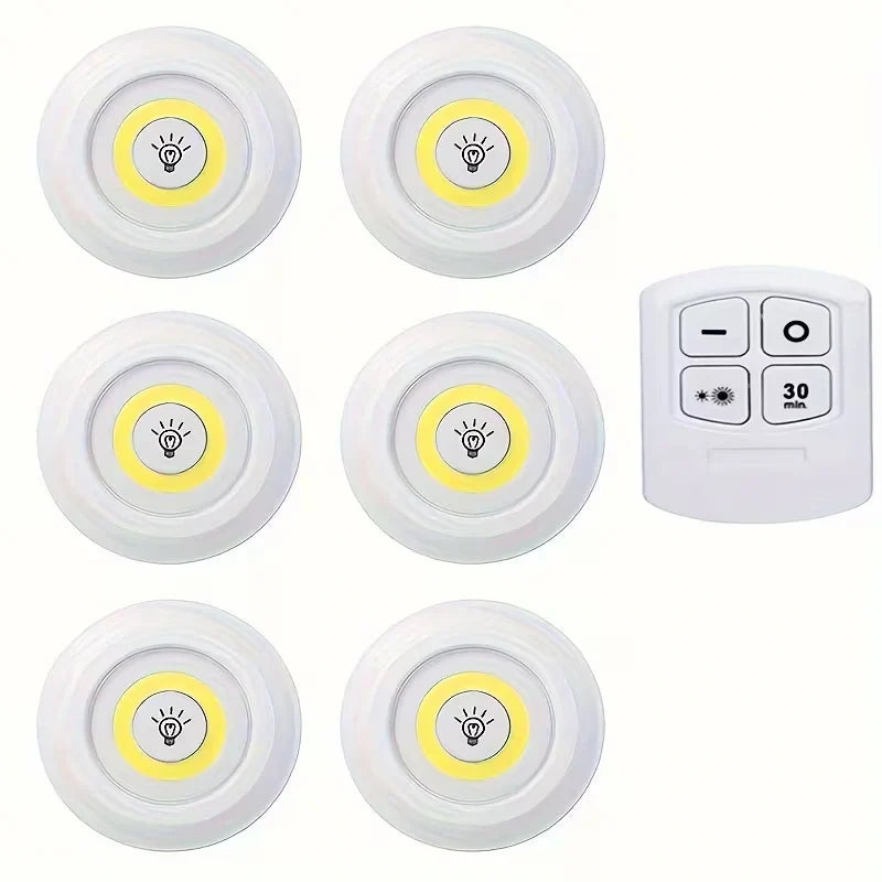 Six round white wireless night lights with yellow centers and light bulb icons, arranged in two rows, with a white remote control on a plain white background.