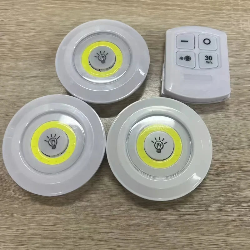Three round light bulbs with yellow accents and a remote control on a wooden surface