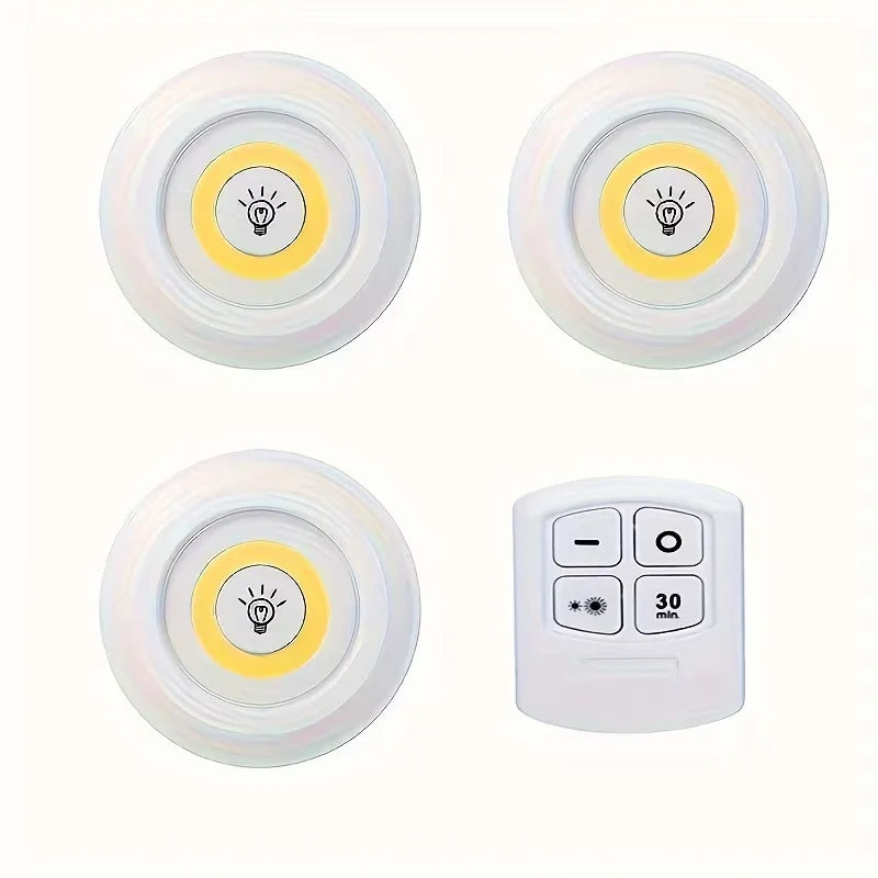 Three round white LED under-cabinet light sensors with yellow light lenses and a white four-button remote control, arranged on a plain white background.